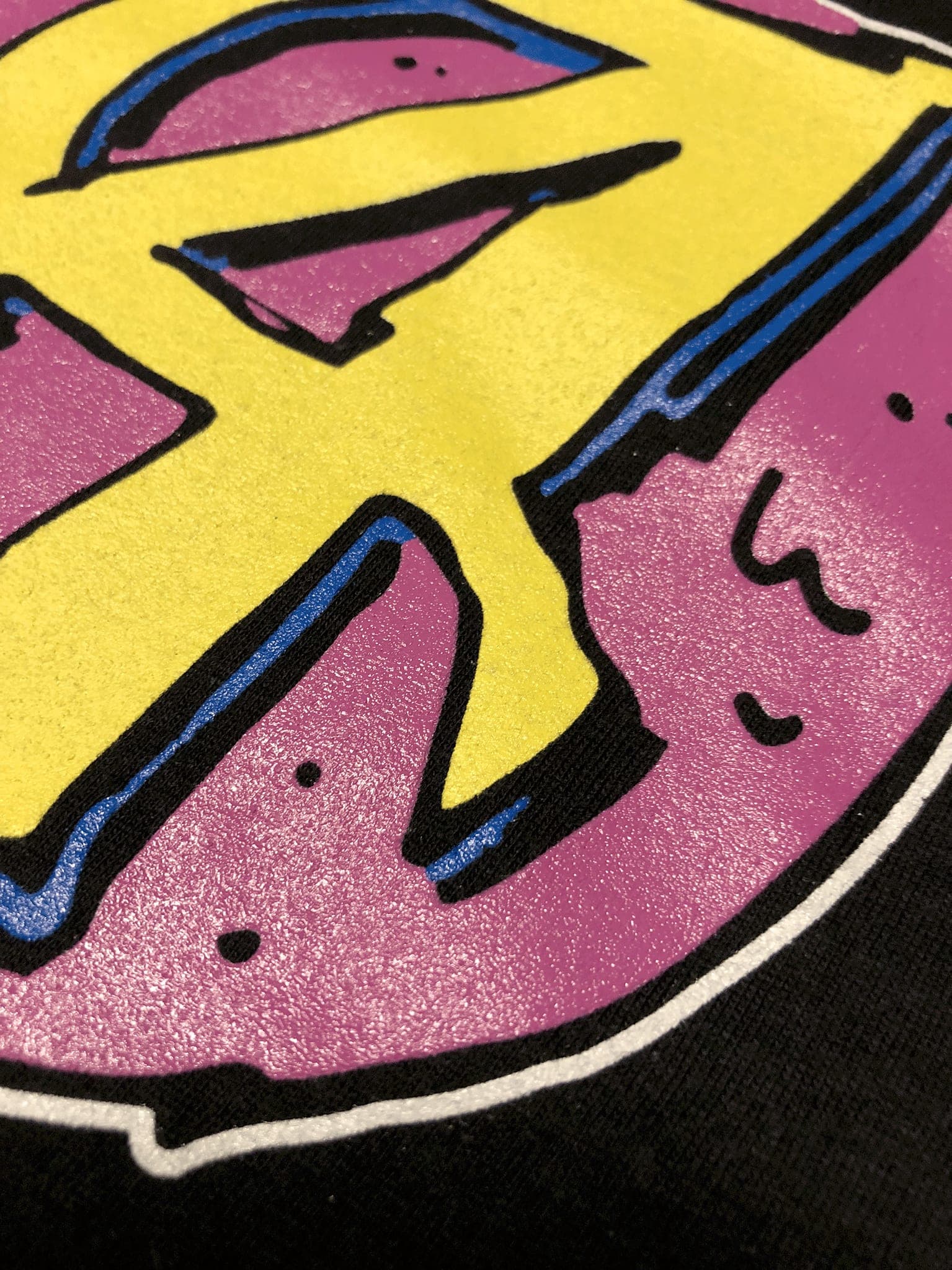 Gros plan sur une impression sérigraphique trois couleurs, relief de l’encre visible sur la maille