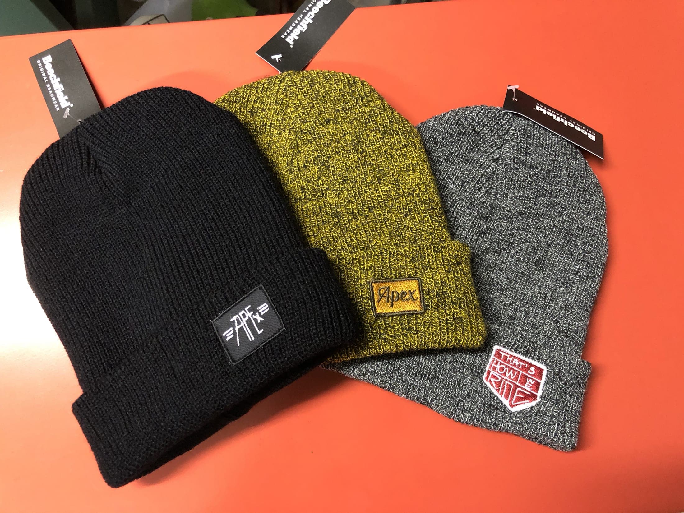 Trois bonnets à étiquette brodée, sur fond orange
