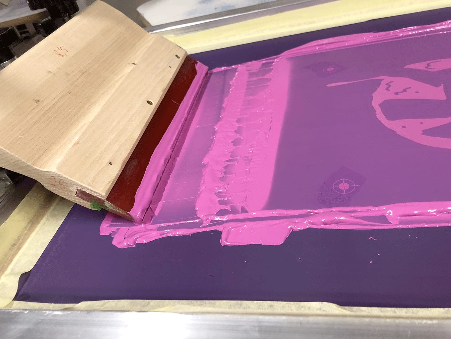 Raclette et encre rose étalée sur un écran de sérigraphie